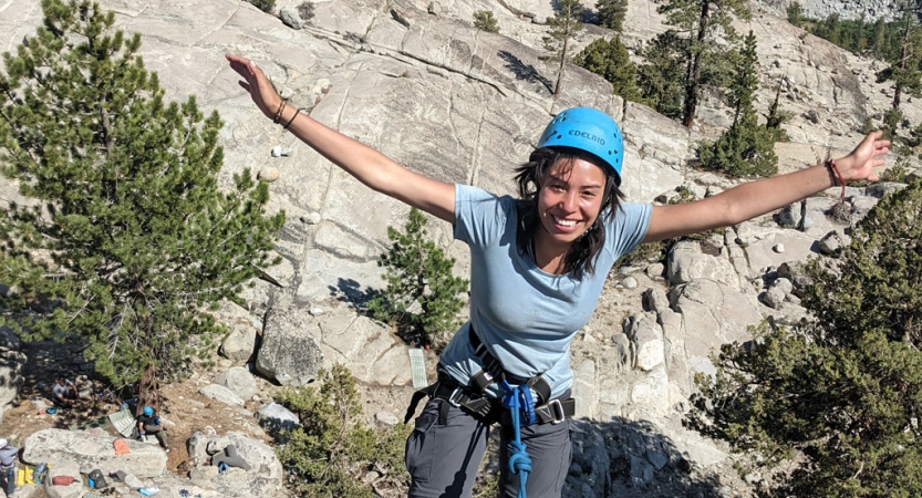 a student wearing rock climbing gear stretches out their hands in celebration
